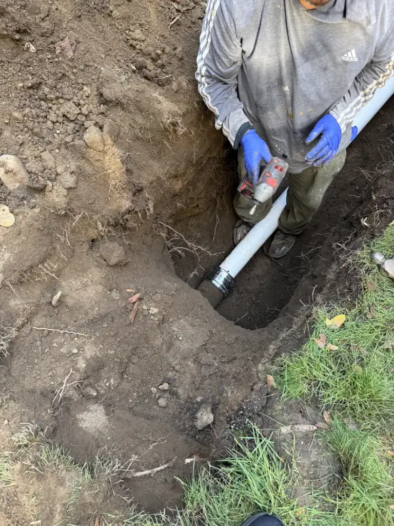 Person repairing sewer line in trench
